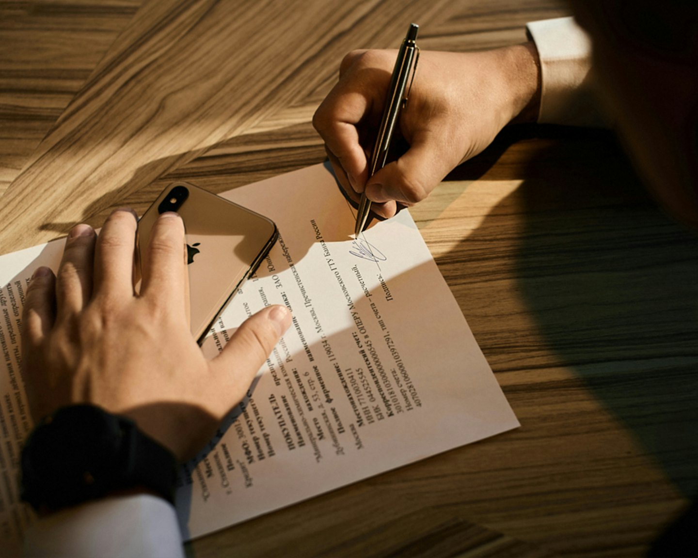 Hands signing a document with a golden pen next to a smartphone.