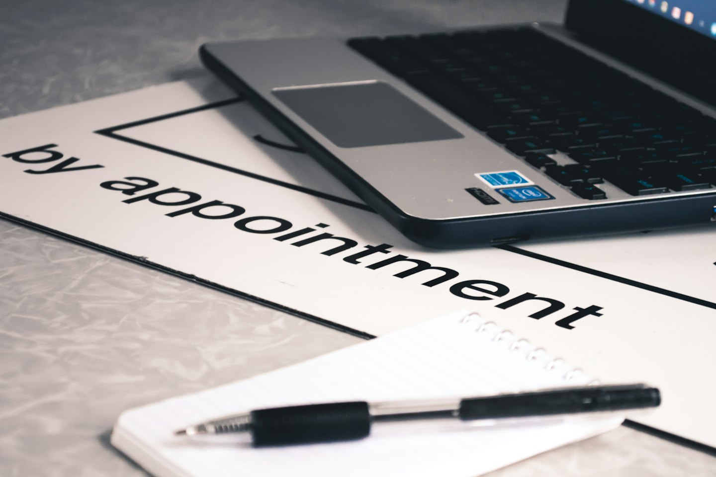 Laptop, notebook, and pen on a desk with an 'by appointment' sign.
