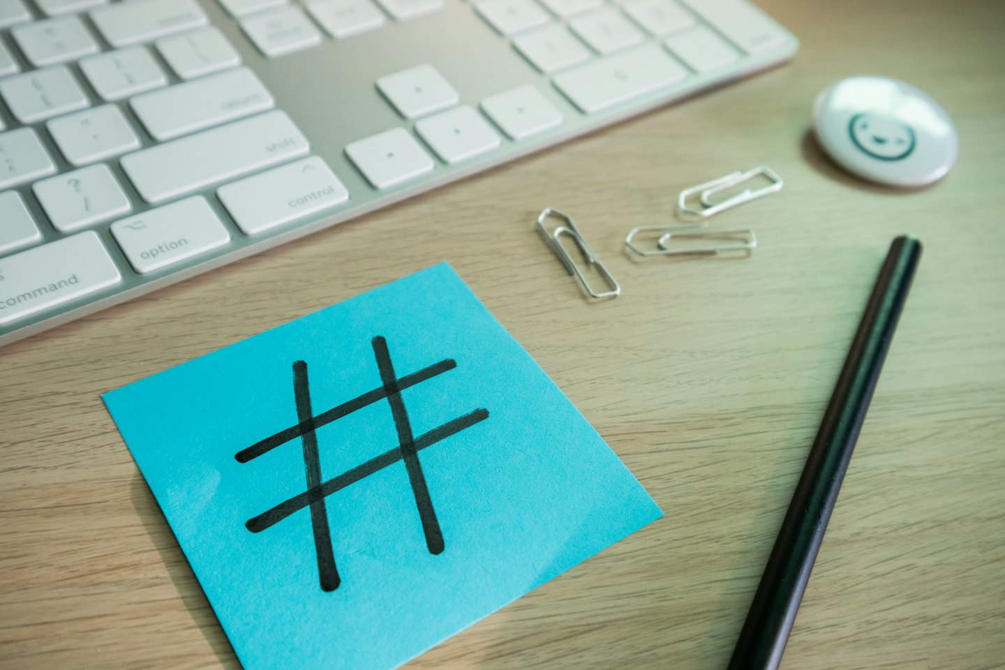 Blue sticky note with hashtag symbol on wooden desk with keyboard.